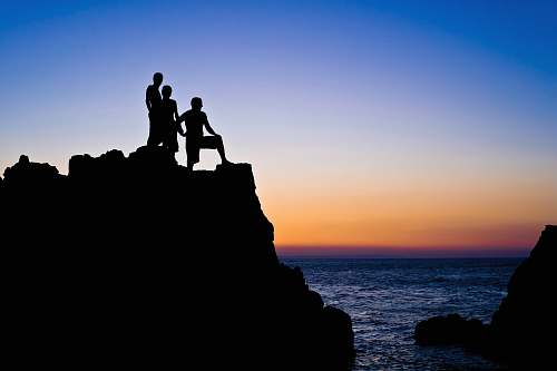 silhouette silhouette of 3 people on top of rocks at beach outdoors