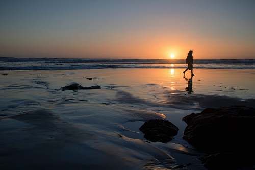 sunset silhouette of person walking on seashore outdoors