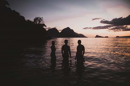 human silhouette of three person standing on calm body of water person