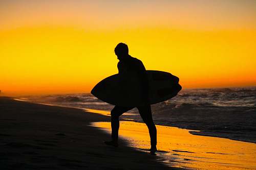 outdoors silhouette photography of man holding surfing board during golden hour ocean