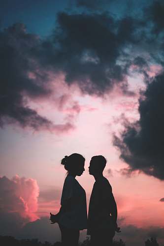 outdoors woman in white T-shirt stands in front of man under grey clouds sky