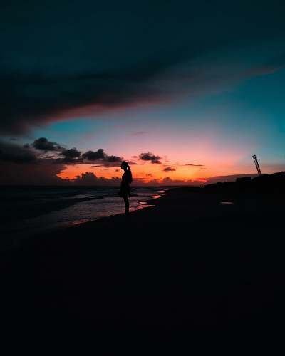 sunset woman standing on shore facing the sea during day outdoors