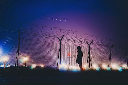 silhouette person's silhouette standing near chain link fence night light