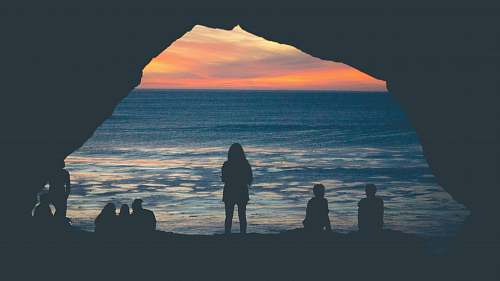 water silhouette of people sitting on seashore watching sunset shoreline