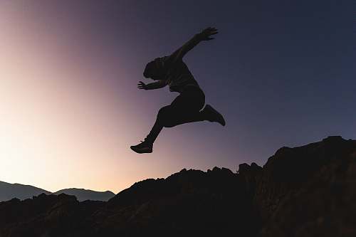 silhouette man jumping above mountains adventure