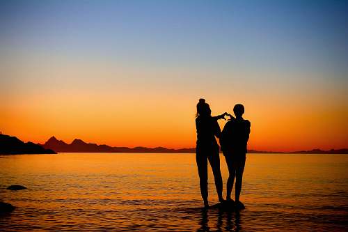 person silhouette of two person standing on seashore during golden hour human