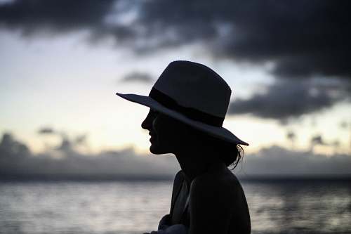 hat silhouette of woman standing beside body of water cowboy hat