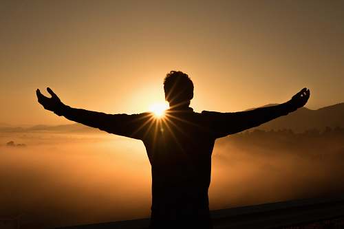 person silhouette photo of man on cliff during sunset orange