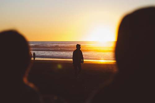 waves silhouette photo of man standing near seashore at sunset ocean