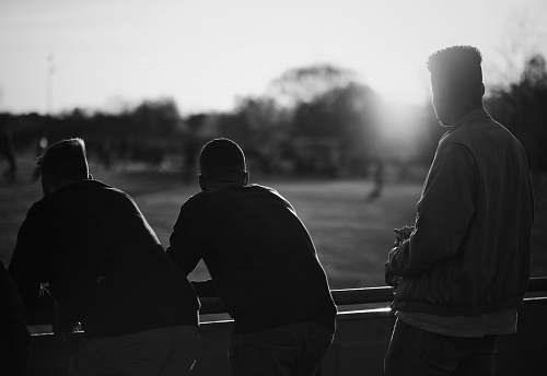 human grayscale photography of three men standing near railings black-and-white