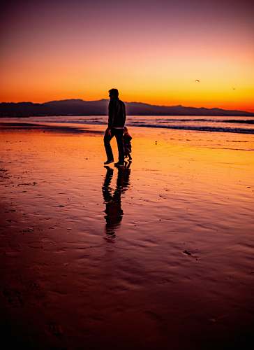 human man and child walk at the seashore during sunset standing
