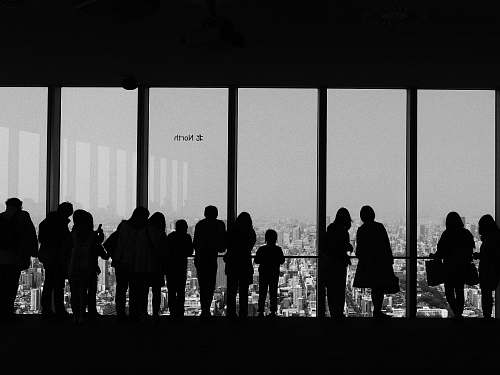 human people overlooking buildings inside room black-and-white