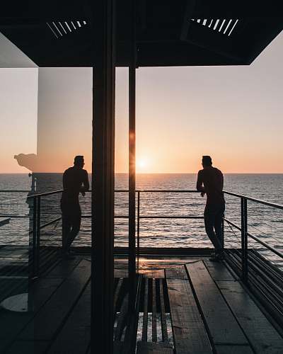 human silhouette of man standing on gray stainless steel railing looking at sunset people