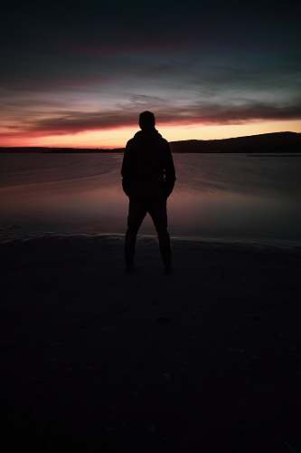 human silhouette of person standing and facing on calm sea during golden hour standing