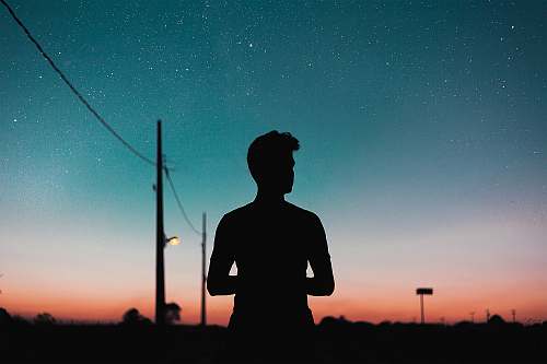 human silhouette of person standing near utility pole during night nature