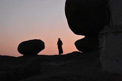 human silhouette of person standing on high ground beside large rock nature