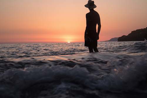 human silhouette of person standing on shallow seashore facing sunset people