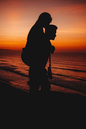 human silhouette of two person across sunset people