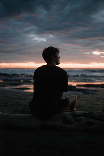 human silhouette photo of man sitting on beach silhouette