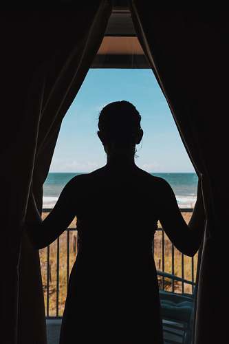 human silhouette photo of woman standing between curtains window