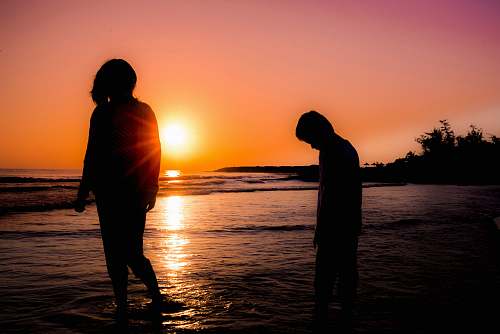 human silhouette photography of boy and girl standing at beach nature