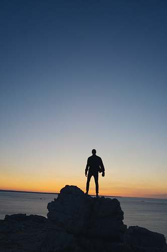 standing silhouette photography of person standing on rock human