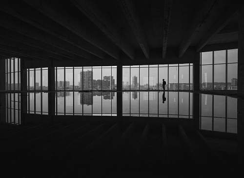 black-and-white grayscale photography of man standing beside window grey
