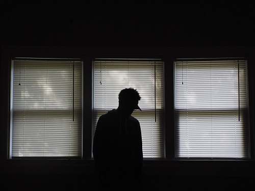 human man standing infront of window blinds person