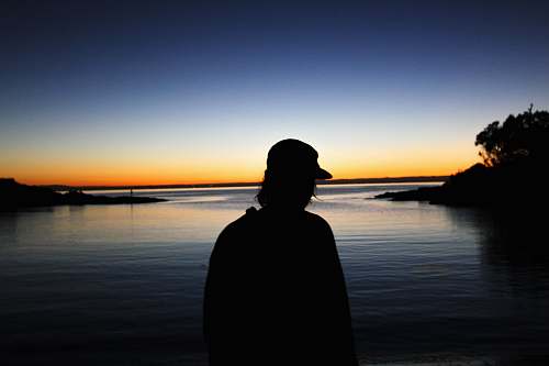 person man standing near body of water silhouette photography sunrise
