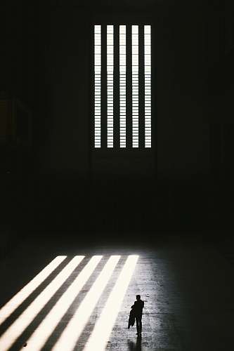 prison man standing near window with window blinds grayscale photography black