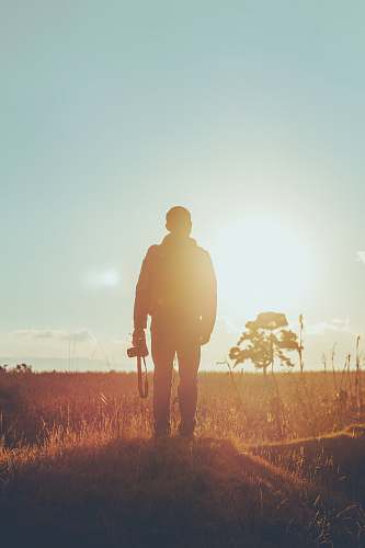 person man standing on dried grass holding camera during golden hour photographer