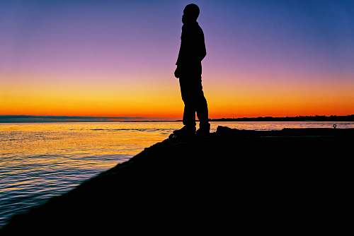 human man standing on shore during golden hour standing
