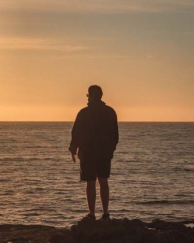 person man standing while overlooking body of water during golden hour human