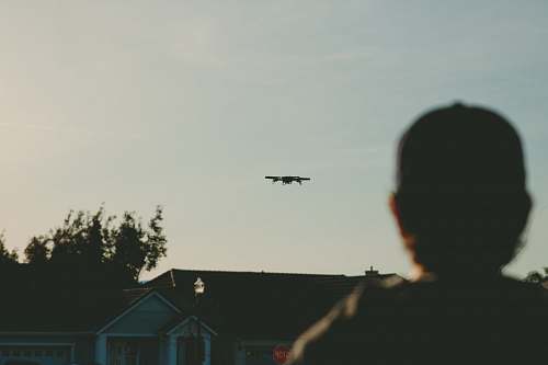 house man standing while watching plane on sky during daytime grey