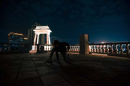 building person in black outfit kneeling near concrete bench night