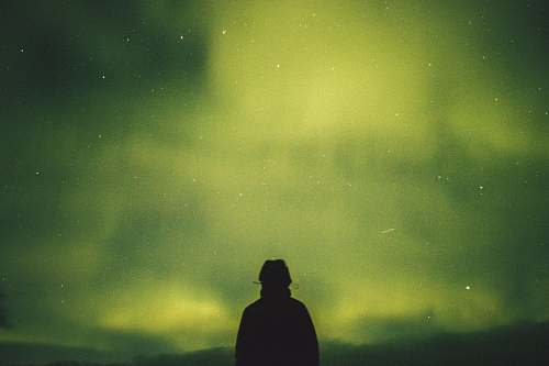 human person standing under green aurora borealis person