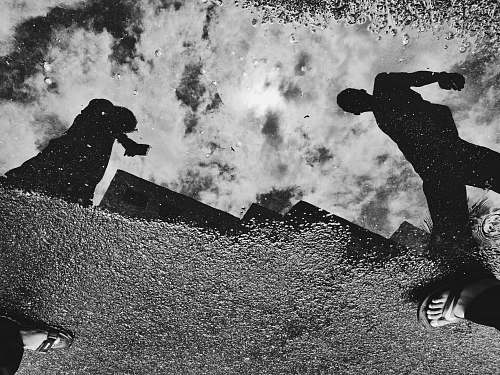 black-and-white reflection of two people on water puddle grey