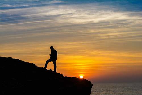 human sihouette of person standing on rock formation during golden hour person