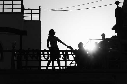 human silhouette of girl standing near man kneeling beside railing black-and-white