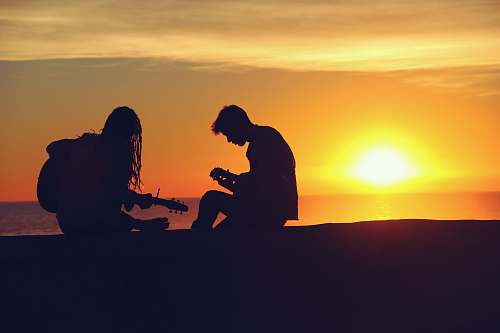 music silhouette of man and woman playing guitars dusk