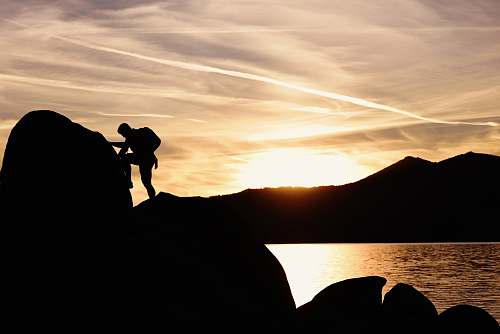 human silhouette of man climbing rock boulder near sea during golden hour outdoors