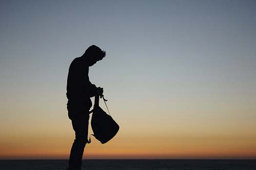 human silhouette of man holding backpack during orange sunset person