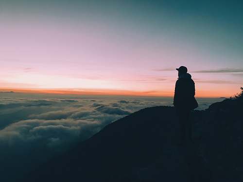 human silhouette of man on hill facing horizon with orange sky person