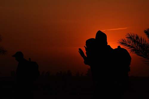 nature silhouette of man sitting on grass under brown sky during nighttime outdoors
