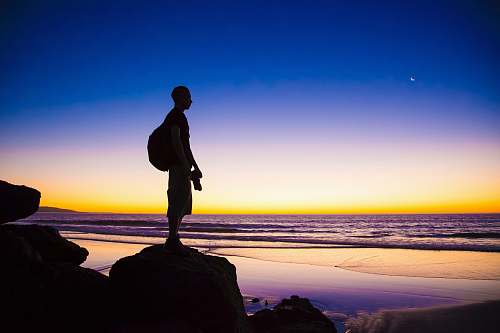 person silhouette of man standing on cliff shore
