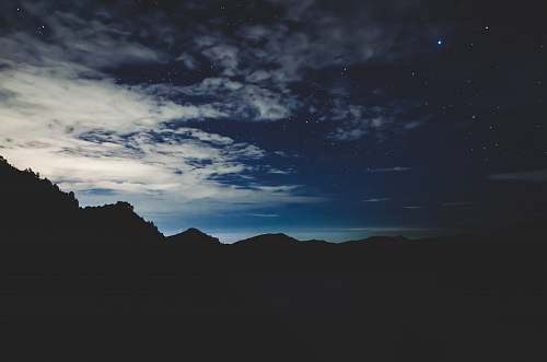 night silhouette of mountain under white clouds stars