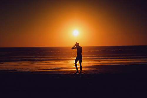 beach silhouette of person beside seashore during sunset ocean