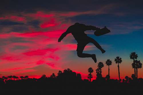 sunset silhouette of person jumping while holding skateboard red