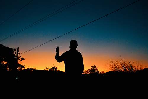 human silhouette of person making peace sign during golden hour person