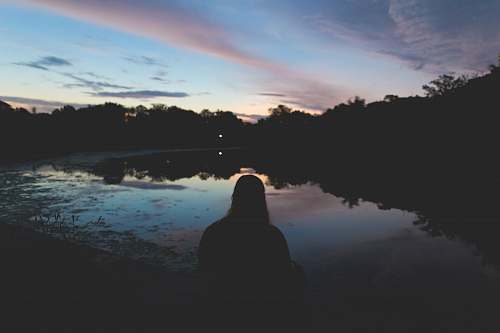trees silhouette of person sitting near body of water sky
